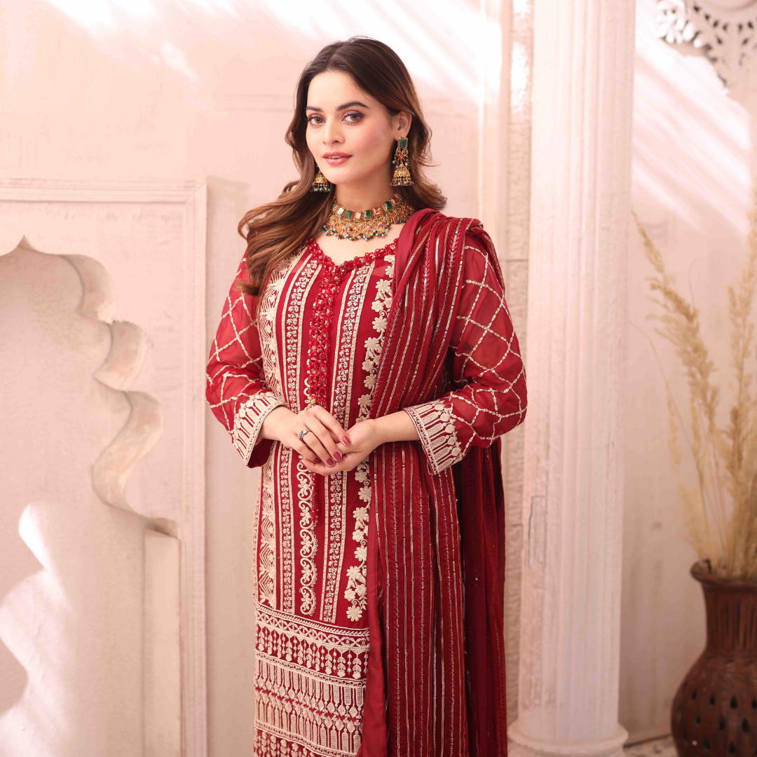 A girl is standing a well lighted place wearing red Embroidered Chiffon Suit with dupatta.