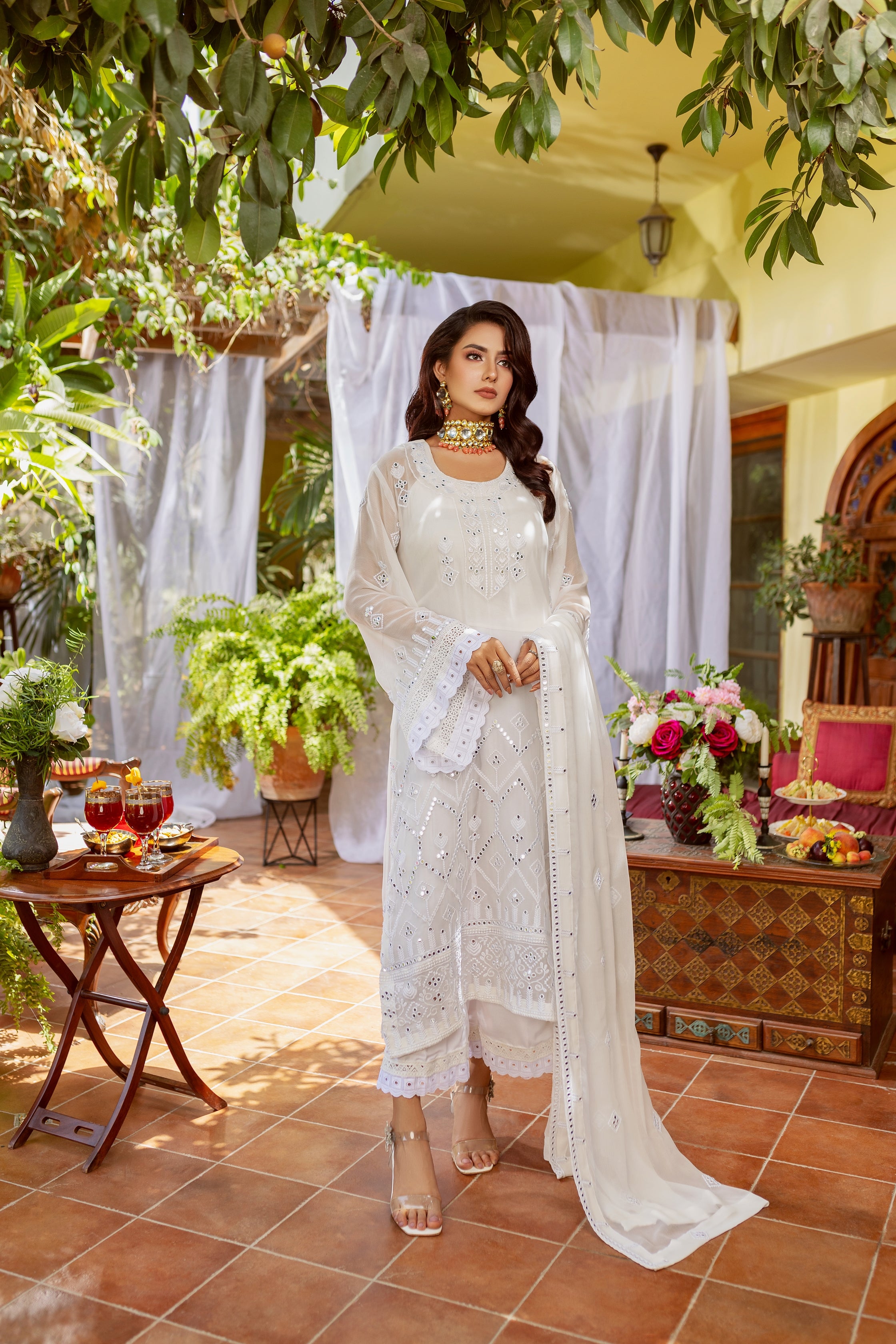 A girl in white embroided chiffon suit standing in outside area of a house.