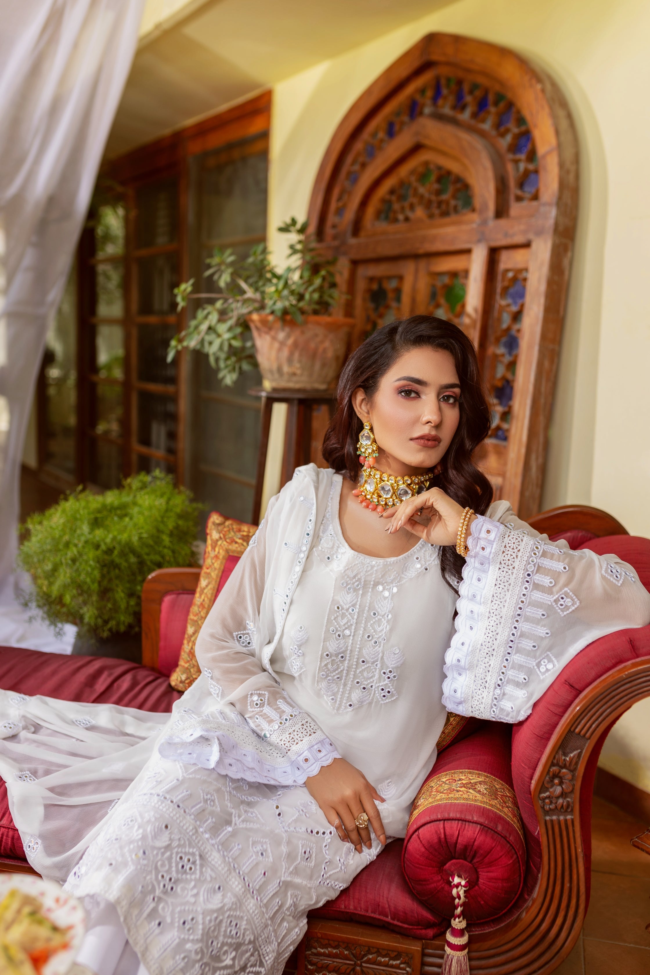 A female model in white embroided chiffon suit sitting on a sofa.