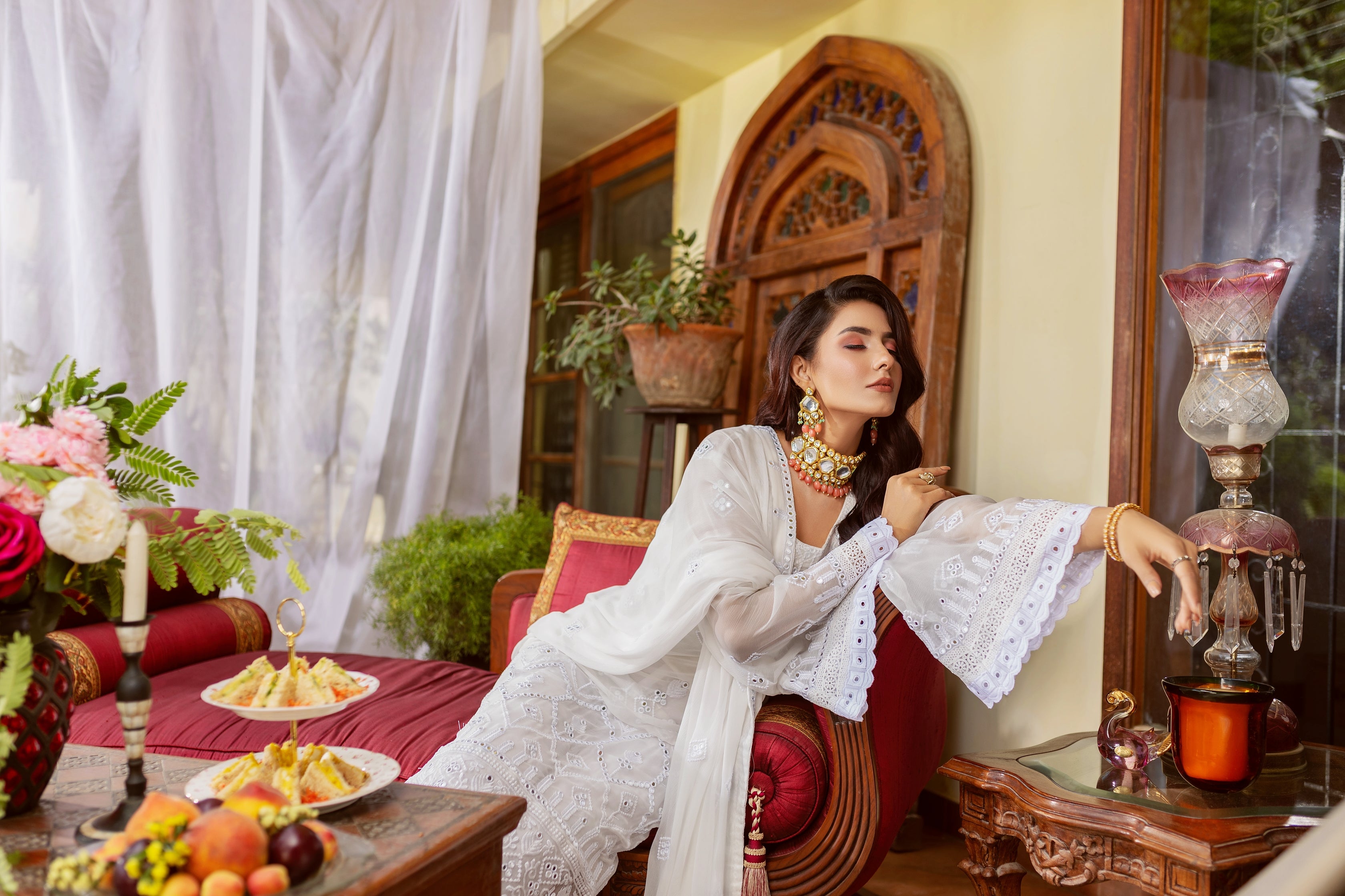 A girl wearing white chiffon suit with dupatta on sofa.