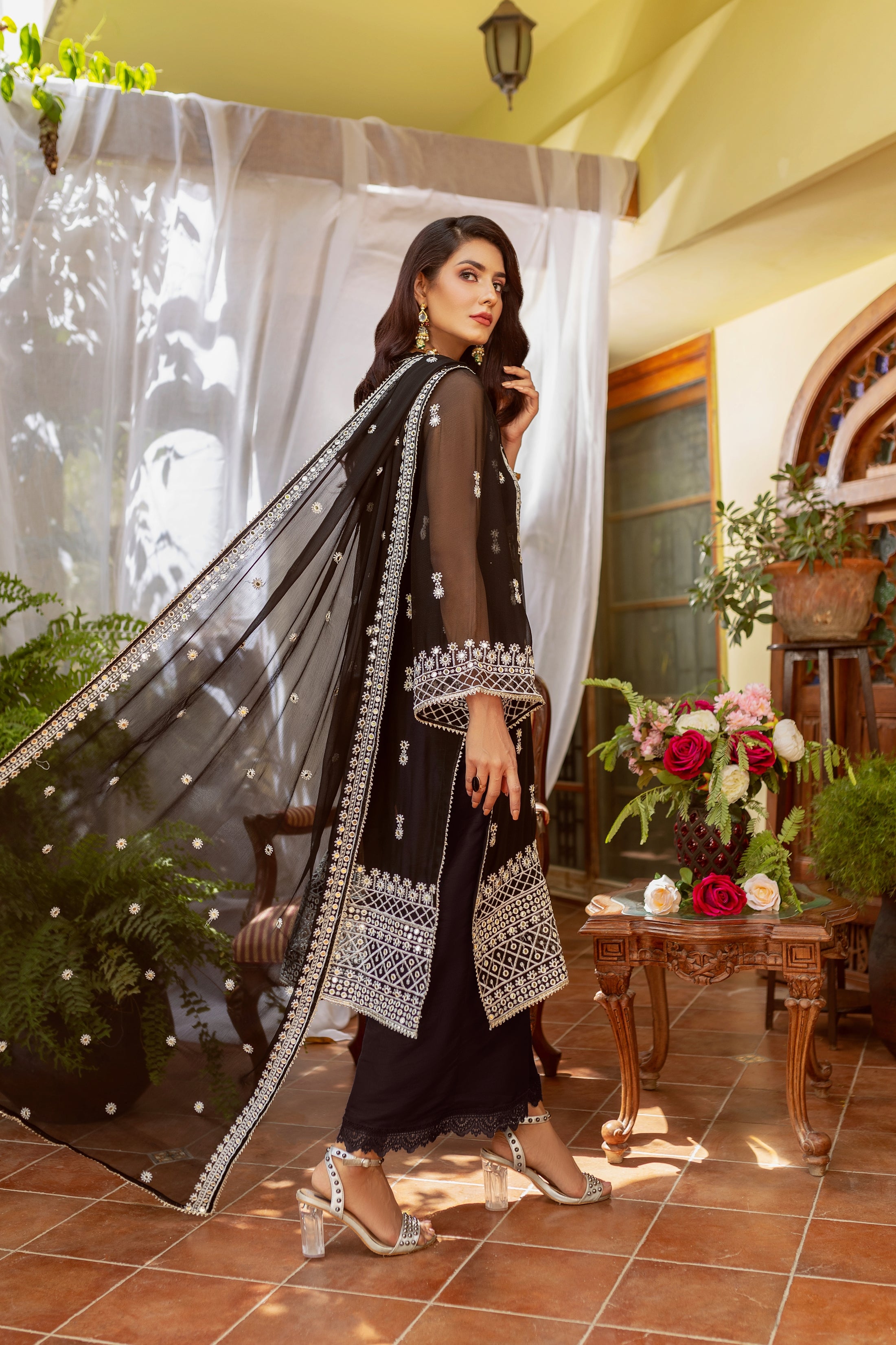 A girl is standing in black embroided chiffon dress with dupatta.