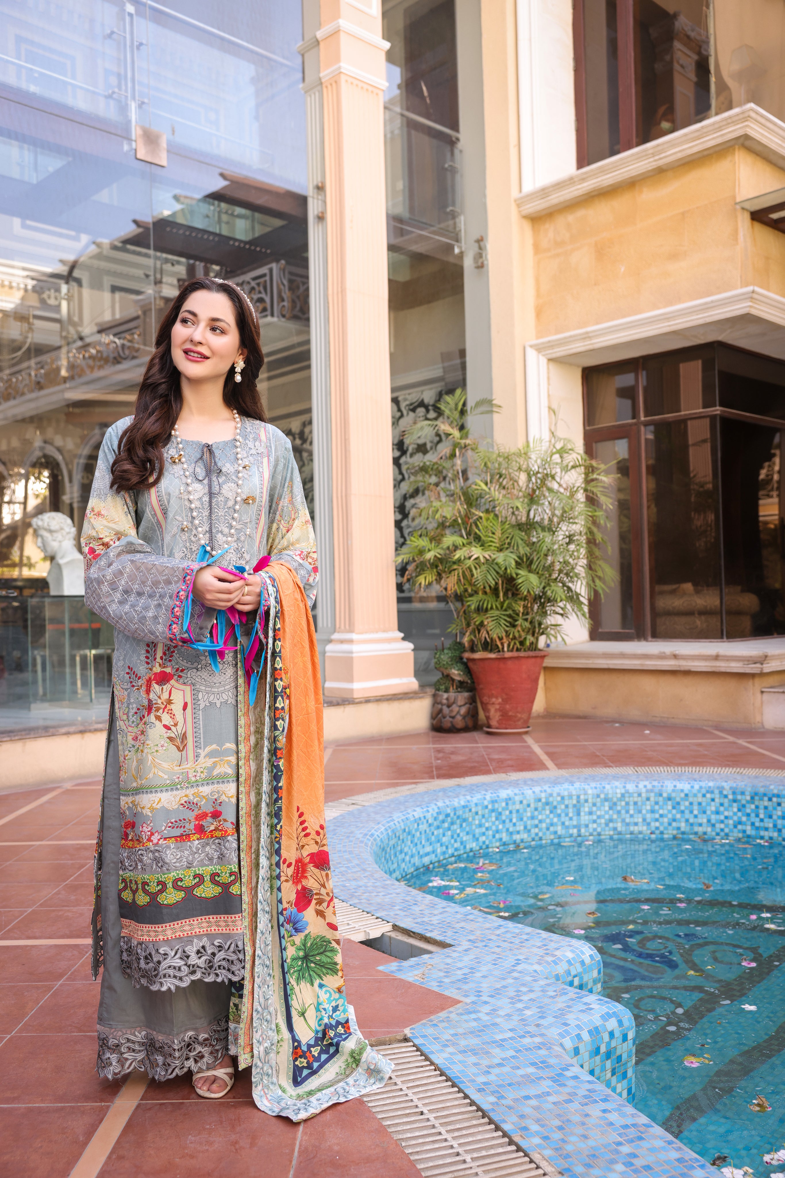 A Girl is standing wearing embroidered organza  suit holding dupatta in her hand along side the a pool.