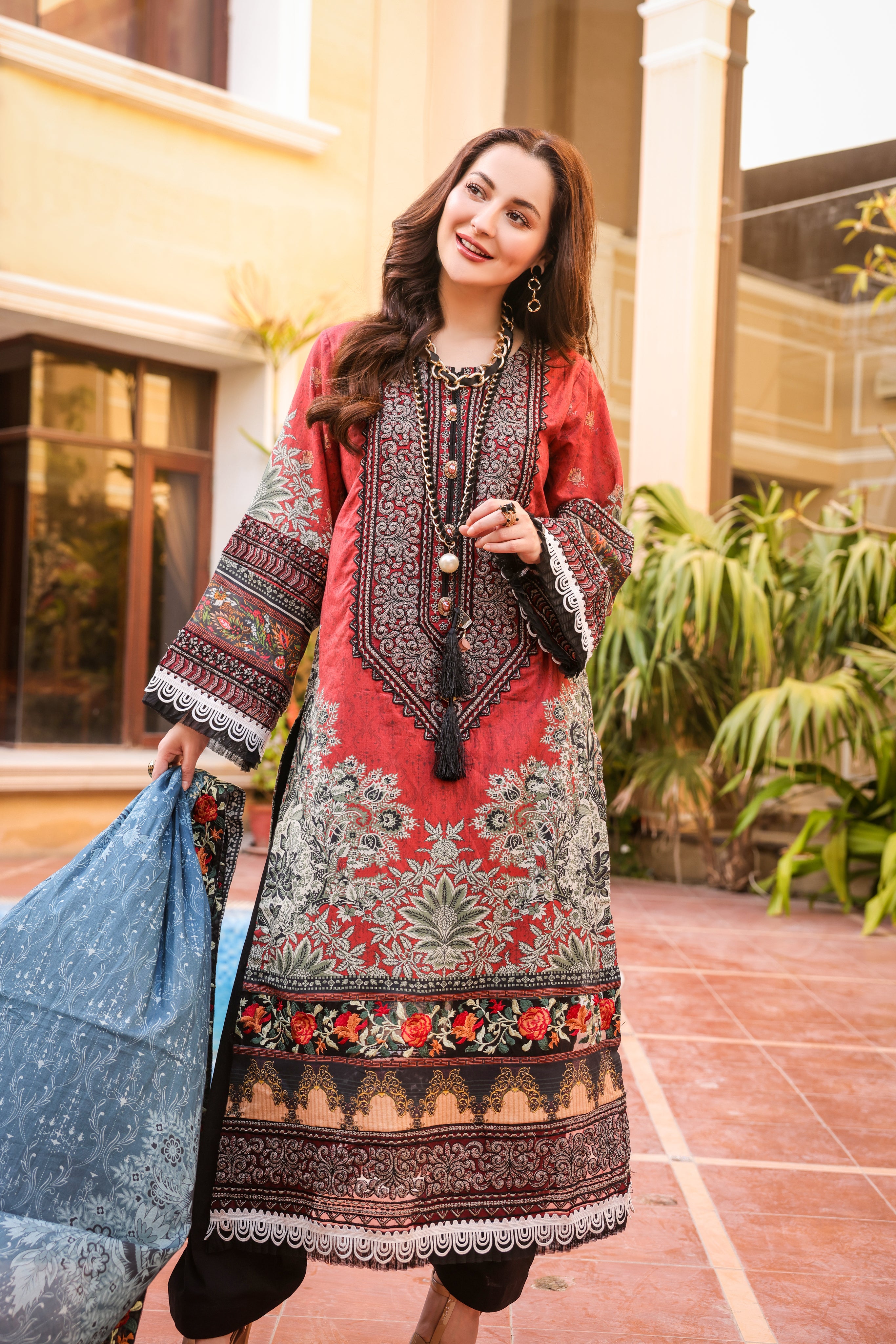 A Girl is standing wearing biking red color embroidered organza suits with dupatta in hand.